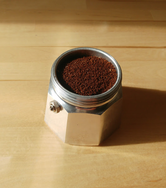 Moka Pot base filled up with water and with coffee grounds in the filter basket